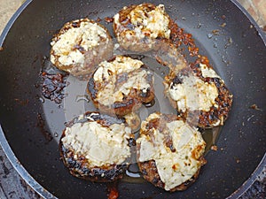 Catalimized onion beef burger with pickled onion and chive cheddar cheese cooking in a non stick pan