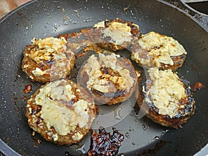 Catalimized onion beef burger with pickled onion and chive cheddar cheese cooking in a non stick pan