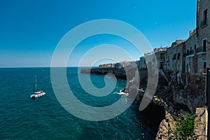 Catamaran boat floating next to Polignano a Mare beachfront at old town. Beautiful coastal town in Apulia is being attracted to