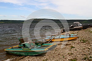 Catamarans on river. Old catamarans and boats lie on a rocky shore of a river bay with steep steep banks in summer