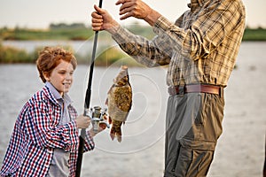 Catch of the day. Cropped grandfather and child boy fishing while on the shore of pond