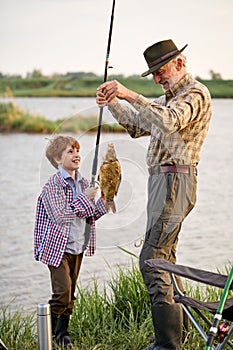Catch of the day. Happy grandfather and child boy fishing while on the shore of pond