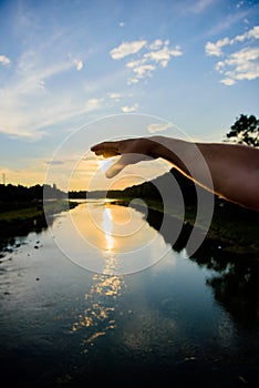 Catch last sunbeam. Male hand pointing at sun in blue sky at evening time admire landscape. River sun reflection