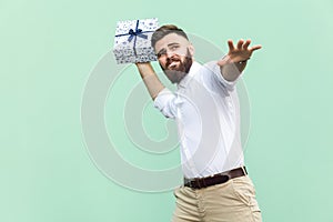 Catch your gift! Young adult man swung and wants to throw off your gift box, isolated on light green background.