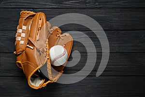 Catcher`s mitt and baseball ball on black wooden table, top view with space for text. Sports game