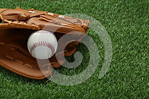 Catcher`s mitt and baseball ball on green grass, space for text. Sports game