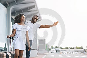 Catching cab. Happy black couple standing at airport parking, calling taxi