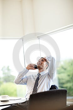 Catching up with a coworker. Handsome young businessman laughing while taking a phone call while sitting indoors.