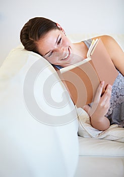 Catching up on her reading. A young woman reading a book while lying on the couch.