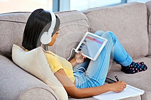 Catching up with the latest tunes. a teenage girl listening to music and using a tablet at home.