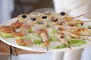 Caterer holding a large plate with small canapes, a selection of finger food prepared for an event