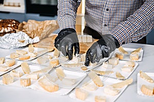 Caterer Preparing Cheese Platters for an Event. Professional caterer arranges various types of cheese on plates, wearing