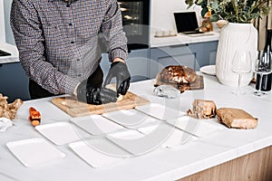Caterer Preparing Cheese Platters for an Event. Professional caterer arranges various types of cheese on plates, wearing
