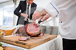 Catering service employee cutting ham