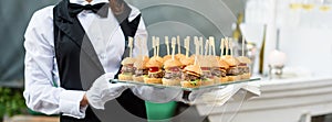 Catering service. Waiter carrying a tray of appetizers. Outdoor party with finger food, mini burgers, sliders. photo