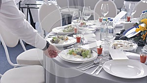 Catering service waiter put plates with dishes on the guests table at a wedding or conference.