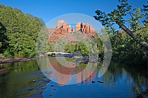 Cathedral Rock reflected in Oak Creek amidst green summer foliage near Sedona, Arizona.