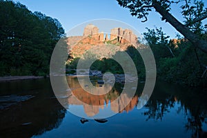 Cathedral Rock reflected in Oak Creek amidst green summer foliage near Sedona, Arizona.