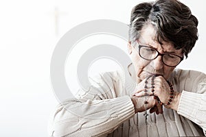 Catholic grandmother in melancholy praying to god with red rosary with cross