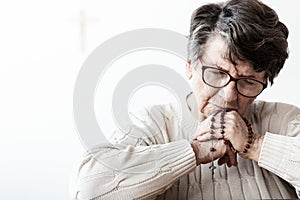 Catholic grandmother in melancholy praying to god with red rosary with cross photo