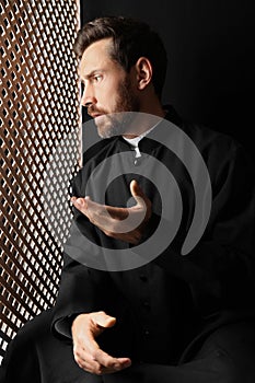 Catholic priest in cassock talking to parishioner in confessional