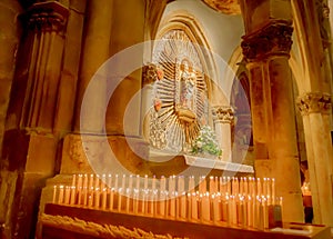 Catholic saint statue at a church shrine with lit candles and church pillars