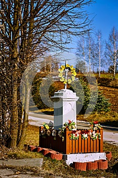 Catholic shrine with flowers and yellow decorations on the background of the field and road