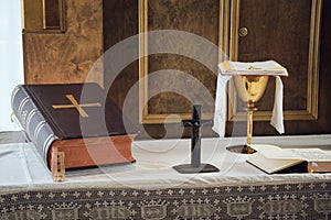 Catholic symbols composition. The Bible, cross and golden chalice on the altar