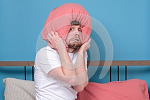 Cauacsian young man with pillow on head in bed being afraid