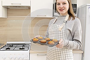 Caucasain woman holding tray with freshly made cupcakes or maffins at the kitchen
