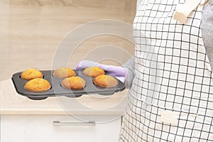 Caucasain woman holding tray with freshly made cupcakes or maffins at the kitchen