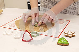 Caucasain woman rolls out the dough with a rolling pin and cuts cookies with cookie cutters at the kitchen