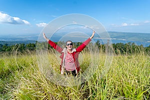 Caucasia woman with red coat and sunglasses spread her arms and stand in the meadow with background of water reservior and