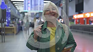 Caucasian 50s senior woman holding passports and boarding passport looking at a camera at airport waiting the flight