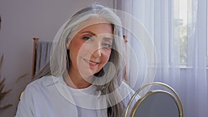 Caucasian 60s aged senior mature lady old gray-haired 50s woman female with mirror smile looking at camera beautiful