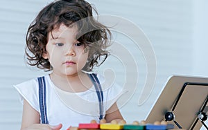 Caucasian adorable cute curly hair little girl wearing white shirt, staying alone, playing toys and tablet in living room at home