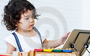 Caucasian adorable cute curly hair little girl wearing white shirt, staying alone, playing toys and tablet in living room at home