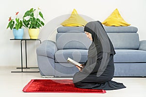A caucasian Adult Muslim woman reads the Quran on a mat at home