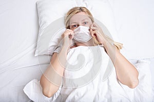 Caucasian adult woman lying in bed with flu, cold and fever, she is sick and wearing face mask