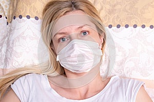 Caucasian adult woman lying in bed with flu, cold and fever, she is sick and wearing face mask