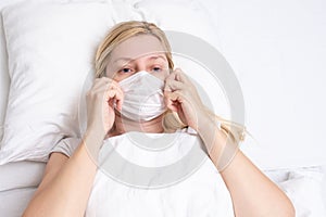 Caucasian adult woman lying in bed with flu, cold and fever, she is sick and wearing face mask