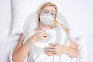 Caucasian adult woman lying in bed with flu, cold and fever, she is sick and wearing face mask