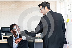 Caucasian and African Businessman wearing a face shield and greeting by elbow bump instead of shaking hands.