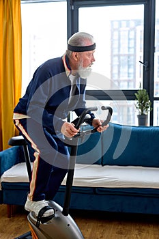 caucasian aged man in mid 70& x27;s exercising on stationary bike at home alone, healthy lifestyle