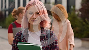 Caucasian alone lonely student girl with pink hair walking smiling at camera holding book walk in city outdoors