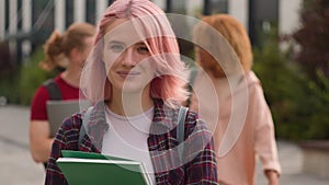 Caucasian alone lonely student girl with pink hair walking smiling at camera holding book walk in city outdoors