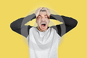 Caucasian angry man screaming out of control while holding his head in desperation. Isolated yellow background