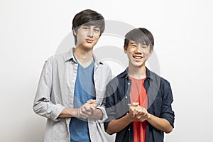 Caucasian and Asian teen boys wear shirt and stand on white background.