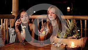 Caucasian and asian women chatting in a bar with drinks, smiling