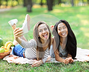 Caucasian and Asian young woman doing selfie and showing tongues